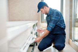 Contemporary technician in workwear installing pipe system by bathtub